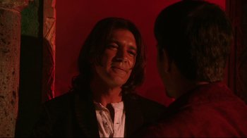 Movie still from “Once Upon a Time in Mexico” (2003), directed by Robert Rodriguez – A man with long hair is smiling for the camera; Close Up shot, Over the shoulder angle