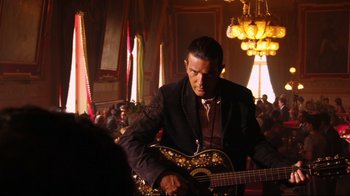 Movie still from “Once Upon a Time in Mexico” (2003), directed by Robert Rodriguez – A man in a suit playing a guitar in front of a group of people; Medium shot, Low angle