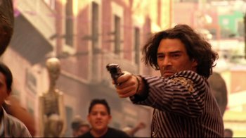 Movie still from “Once Upon a Time in Mexico” (2003), directed by Robert Rodriguez – A man holding a gun while standing next to a statue; Medium shot, Over the shoulder angle