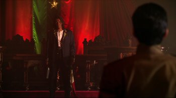 Movie still from “Once Upon a Time in Mexico” (2003), directed by Robert Rodriguez – A man wearing a suit and tie standing in front of a stage; Medium shot, Low angle