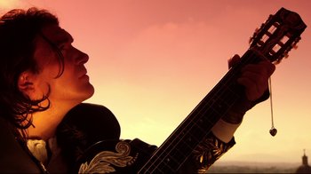Movie still from “Once Upon a Time in Mexico” (2003), directed by Robert Rodriguez – A man holding a guitar in front of a pink sky; Close Up shot, Low angle