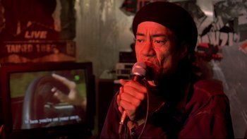 Movie still from “Once Were Warriors” (1994), directed by Lee Tamahori – A man holding a microphone in front of a television; Close Up shot, Low angle