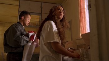 Movie still from “Once Were Warriors” (1994), directed by Lee Tamahori – A woman with long hair standing in a kitchen next to a boy; Medium shot, Low angle