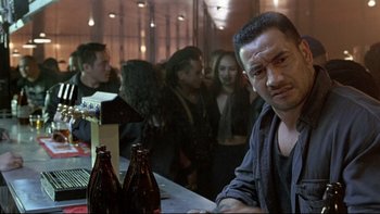 Movie still from “Once Were Warriors” (1994), directed by Lee Tamahori – A man sitting at a bar with a group of people behind him; Close Up shot, Over the shoulder angle