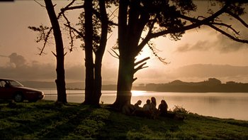 Movie still from “Once Were Warriors” (1994), directed by Lee Tamahori – A group of people sitting under a tree near a body of water; Extreme Wide shot, Low angle