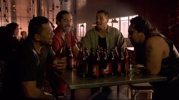 Movie still from “Once Were Warriors” (1994), directed by Lee Tamahori – A group of men sitting at a table with bottles of beer; Medium shot, High angle