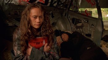 Movie still from “Once Were Warriors” (1994), directed by Lee Tamahori – A young woman with long brown hair is holding her hands on her chest while a young man sleeps in the back of a car; Close Up shot, Low angle