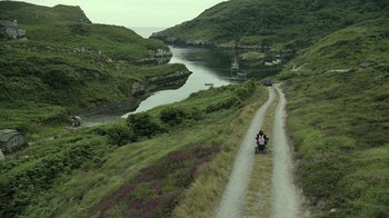 Movie still from “Ondine” (2009), directed by Neil Jordan – Two people riding a motorcycle down a dirt road near a body of water; Extreme Wide shot, High angle