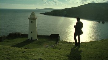 Movie still from “Ondine” (2009), directed by Neil Jordan – A man standing next to a white lighthouse on a grassy hill; Extreme Wide shot, Low angle