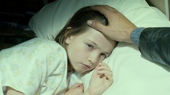 Movie still from “Ondine” (2009), directed by Neil Jordan – A young girl laying in a bed with a person touching her head; Close Up shot, High angle
