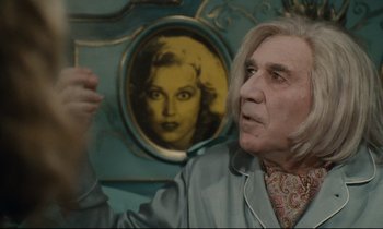 Movie still from “One Hundred and One Nights” (1995), directed by Agnès Varda – An older man in front of a picture of an old woman; Medium shot, Over the shoulder angle