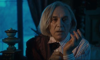 Movie still from “One Hundred and One Nights” (1995), directed by Agnès Varda – An older man with long white hair wearing a striped shirt; Close Up shot, Over the shoulder angle