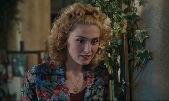 Movie still from “One Hundred and One Nights” (1995), directed by Agnès Varda – A woman with blonde curly hair sitting in front of a plant; Close Up shot, Over the shoulder angle