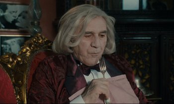 Movie still from “One Hundred and One Nights” (1995), directed by Agnès Varda – An older man holding a fork in his hand; Medium shot, Over the shoulder angle