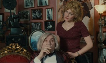 Movie still from “One Hundred and One Nights” (1995), directed by Agnès Varda – A man sitting in a chair next to a woman in front of a mirror; Medium shot, Over the shoulder angle