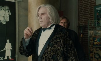 Movie still from “One Hundred and One Nights” (1995), directed by Agnès Varda – An older man in a black and gold jacket; Medium shot, Over the shoulder angle