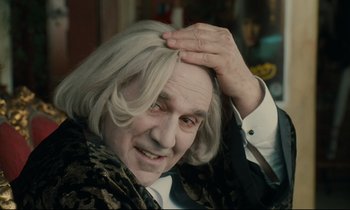 Movie still from “One Hundred and One Nights” (1995), directed by Agnès Varda – An older man with a white wig is holding his head; Close Up shot, Over the shoulder angle