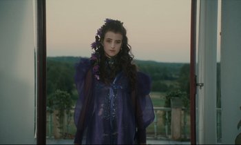 Movie still from “One Hundred and One Nights” (1995), directed by Agnès Varda – A woman in a purple dress with purple flowers in her hair; Medium shot, Low angle