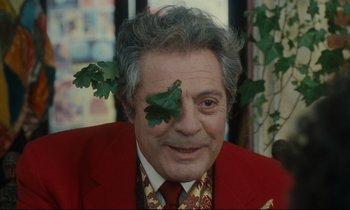 Movie still from “One Hundred and One Nights” (1995), directed by Agnès Varda – An older man in a red jacket with a leaf on his face; Close Up shot, Over the shoulder angle