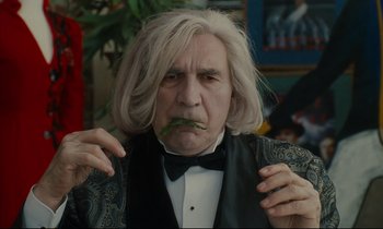 Movie still from “One Hundred and One Nights” (1995), directed by Agnès Varda – An older man with long white hair wearing a black bow tie; Close Up shot, Over the shoulder angle