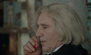Movie still from “One Hundred and One Nights” (1995), directed by Agnès Varda – An older man with white hair is holding a flower; Close Up shot, Over the shoulder angle