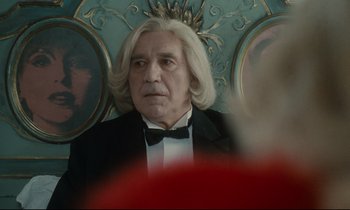 Movie still from “One Hundred and One Nights” (1995), directed by Agnès Varda – An older man with long white hair wearing a tuxedo; Close Up shot, Over the shoulder angle