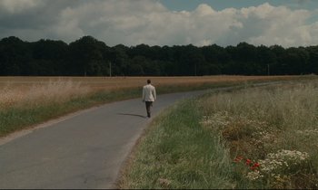 Movie still from “One Hundred and One Nights” (1995), directed by Agnès Varda – A man walking down a road in the middle of a field; Extreme Wide shot, High angle