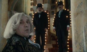 Movie still from “One Hundred and One Nights” (1995), directed by Agnès Varda – A man in a top hat and suit standing in front of two other men; Medium shot, Low angle