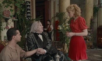 Movie still from “One Hundred and One Nights” (1995), directed by Agnès Varda – A woman in a red polka dot dress talking to a man in a wheelchair; Medium shot, Over the shoulder angle