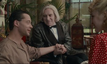 Movie still from “One Hundred and One Nights” (1995), directed by Agnès Varda – Two men sitting in a living room holding hands; Medium shot, Over the shoulder angle