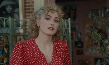 Movie still from “One Hundred and One Nights” (1995), directed by Agnès Varda – A woman in a polka dot dress is posing for a picture; Close Up shot, Over the shoulder angle