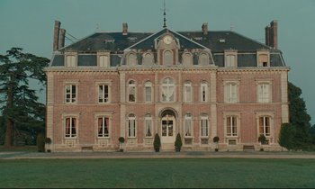 Movie still from “One Hundred and One Nights” (1995), directed by Agnès Varda – A large brick building with a clock on it's face; Extreme Wide shot, Low angle