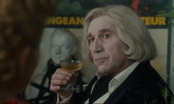 Movie still from “One Hundred and One Nights” (1995), directed by Agnès Varda – A man in a suit holding up a glass of wine; Close Up shot, Over the shoulder angle