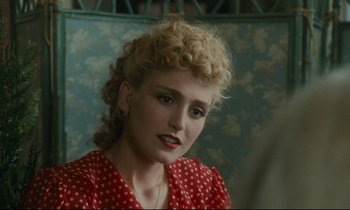 Movie still from “One Hundred and One Nights” (1995), directed by Agnès Varda – A woman in a red polka dot dress with blonde curly hair; Close Up shot, Over the shoulder angle