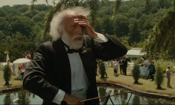 Movie still from “One Hundred and One Nights” (1995), directed by Agnès Varda – An older man in a tuxedo holding his hand up to his head; Medium shot, Over the shoulder angle