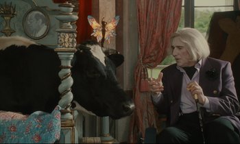 Movie still from “One Hundred and One Nights” (1995), directed by Agnès Varda – An older woman sitting in front of a black and white cow; Medium shot, Over the shoulder angle