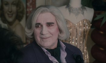 Movie still from “One Hundred and One Nights” (1995), directed by Agnès Varda – An old man with a white wig and a black jacket; Close Up shot, Over the shoulder angle