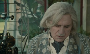 Movie still from “One Hundred and One Nights” (1995), directed by Agnès Varda – An older man with long white hair wearing a suit and tie; Close Up shot, Low angle