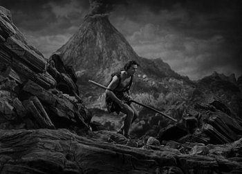 Movie still from “One Million B.C.” (1940), directed by Hal Roach Jr. – A man is holding a spear in a rocky area; Wide shot, Low angle
