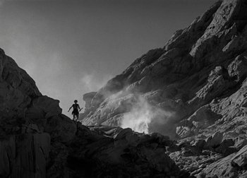 Movie still from “One Million B.C.” (1940), directed by Hal Roach Jr. – A man standing on a rocky mountain side holding a pole; Extreme Wide shot, Low angle