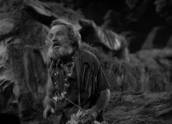 Movie still from “One Million B.C.” (1940), directed by Hal Roach Jr. – An old man with long hair and a long beard is standing in front of some rocks; Medium shot, Low angle