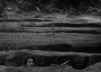 Movie still from “One Million B.C.” (1940), directed by Hal Roach Jr. – A man is sitting in a hole in the ground; Wide shot, High angle