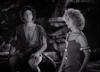 Movie still from “One Million B.C.” (1940), directed by Hal Roach Jr. – A man and a woman sitting next to each other in front of rocks; Medium shot, High angle