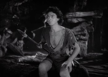 Movie still from “One Million B.C.” (1940), directed by Hal Roach Jr. – A man holding an axe while sitting on a tree stump; Medium shot, High angle