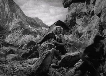 Movie still from “One Million B.C.” (1940), directed by Hal Roach Jr. – A woman sitting on top of a rock with an eagle on her arm; Wide shot, High angle