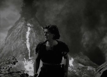 Movie still from “One Million B.C.” (1940), directed by Hal Roach Jr. – A black and white photo of a woman standing in front of an erupting volcano; Medium shot, Low angle