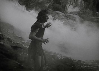 An old photo of a woman standing in front of a waterfall