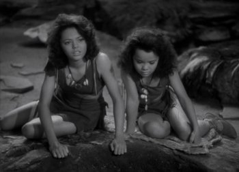 Movie still from “One Million B.C.” (1940), directed by Hal Roach Jr. – Two young girls sitting on the ground looking at the camera; Medium shot, High angle