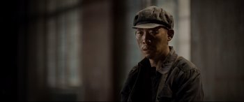 Movie still from “One Second” (2020), directed by Yimou Zhang – A man wearing a hat and a black jacket; Close Up shot, Low angle