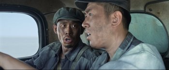 Movie still from “One Second” (2020), directed by Yimou Zhang – Two asian men are talking and one of them is looking at the camera; Close Up shot, Low angle